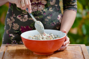 Female hands with a spoon stir chestnut fruit salad in an orange bowl Female hands with a spoon stir chestnut fruit salad in an orange bowl
